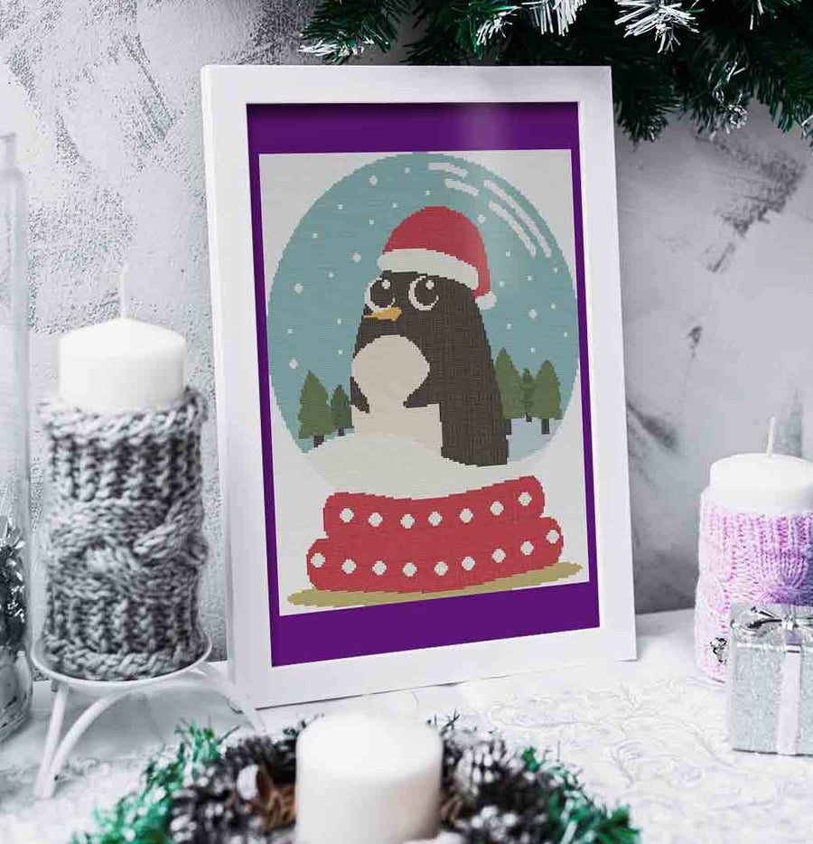 A stitched and framed preview of the counted cross stitch pattern Joyful Penguin: Counted Cross Stitch Pattern and Kit
