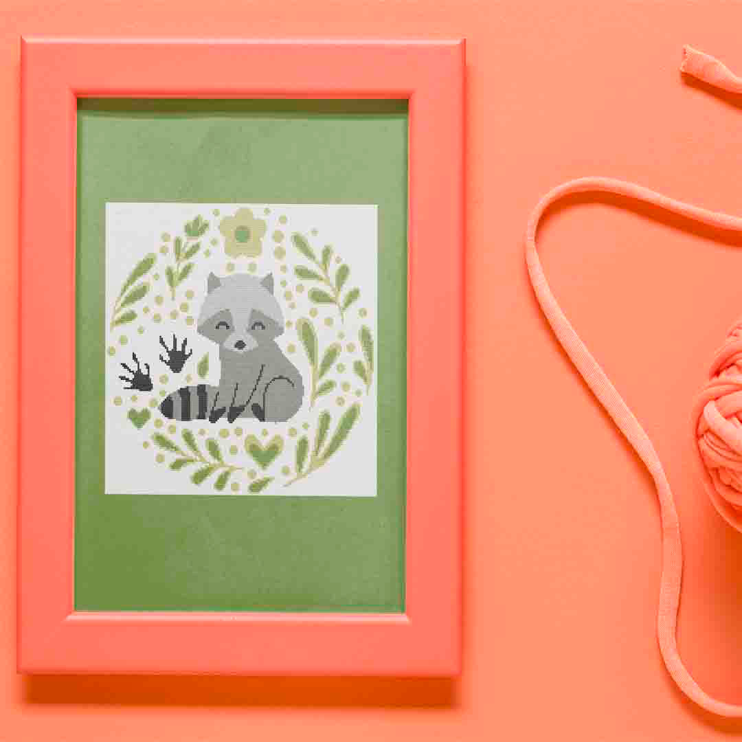 Stitched and framed preview of The Cutest Trash Panda Counted Cross Stitch Pattern and Kit